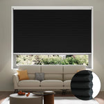 A living room with a beige sofa, yellow and orange cushions, a coffee table, and a large window covered by a closed black cellular blackout shade; an inset shows a close-up of the shade’s honeycomb structure.