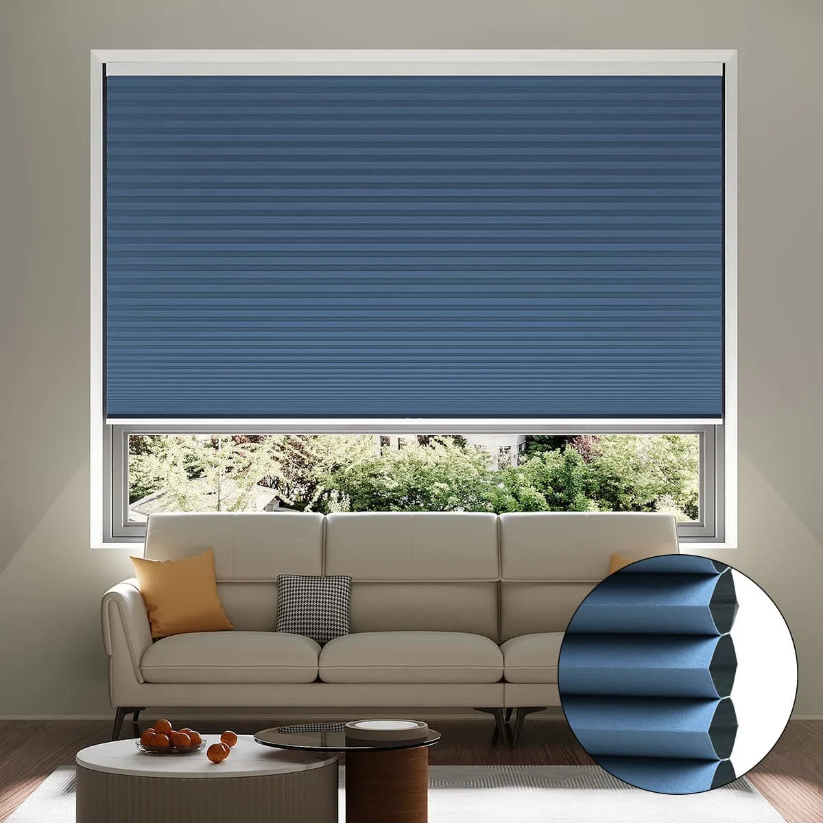 A living room with a beige sofa, cushions, and a coffee table. The window features a partially raised blue cellular shade, with an inset showing a close-up of its honeycomb structure. Trees are visible outside.