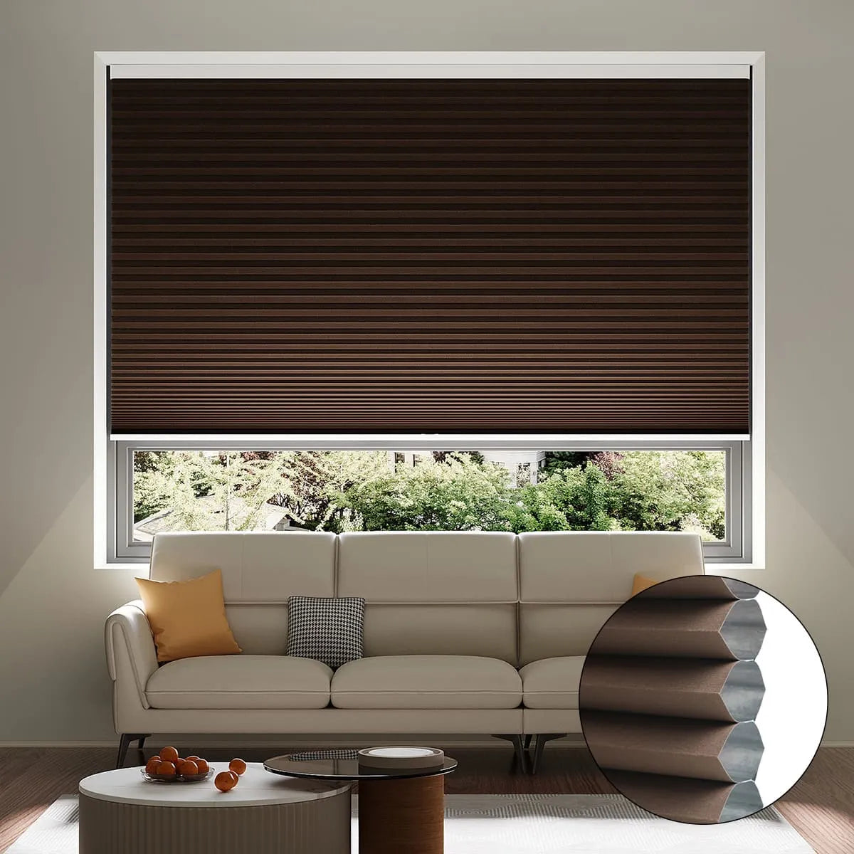 A living room with a beige sofa and orange pillows sits in front of a window with partially closed dark brown honeycomb blinds; an inset shows a close-up of the blind’s cellular structure.