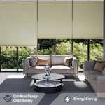 Modern living room with large windows covered by beige cordless blinds. Two sofas with cushions and a round coffee table sit on a rug. Icons indicate child safety and energy-saving features. Green trees are visible outside.