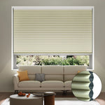 A living room with a beige pleated cellular window shade, cream sofa with yellow and gray pillows, a small coffee table, and a window view of greenery outside. An inset shows a close-up of the shade’s honeycomb structure.